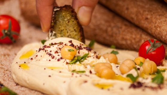 Una mano intinge un pezzo di falafel nell'hummus condito con olio e pomodorini