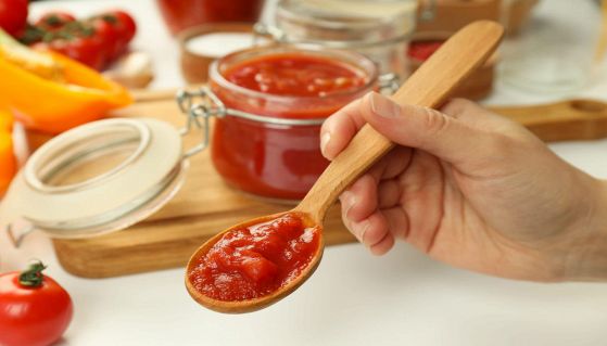 Barattolo di salsa al pomodoro con persona che ne prende un cucchiaio
