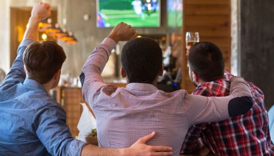 Tre clienti di una pizzeria esultano guardando la partita in tv bevendo birra