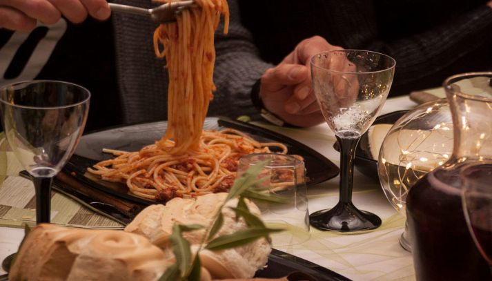 Persona serve spaghetti su tavolo imbandito