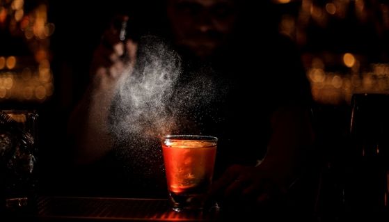 Bartender spruzza essenza su un cocktail con ghiaccio sul bancone