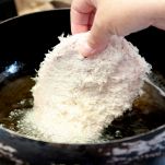 Mano immerge cotoletta di maiale nell'olio bollente