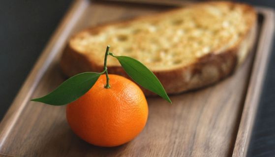 Il mandarino iperrealistico dello Chef Heston Blumenthal su un vassoio di legno accanto ad una fetta di pane