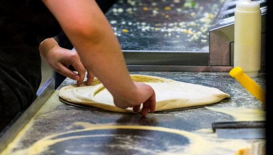 Cucina del ristorante con pizzaiola che stende la pizza