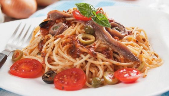 Un piatto di spaghetti alla puttanesca con pomodori, olive nere e acciughe