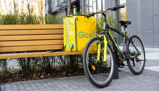 Una bici e uno zaino Glovo poggiati ad una panchina vuota