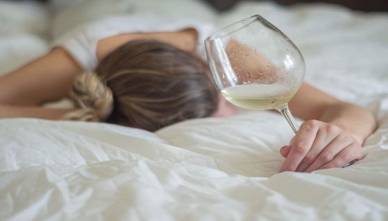 Donna ubriaca a letto con un calice di vino