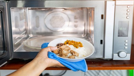 Mano femminile apre il microonde per scaldare il cibo