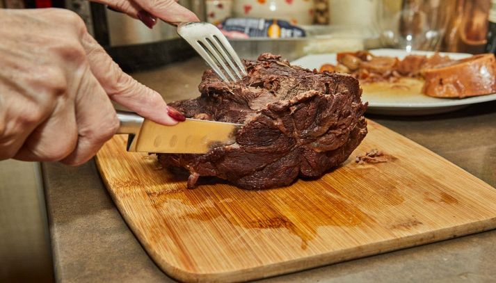 Mani femminili affettano un pezzo di carne cotta