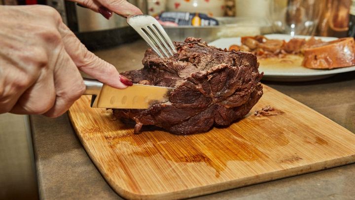 Mani femminili affettano un pezzo di carne cotta