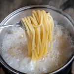 Forchetta di linguine lessate sopra a una pentola di acqua bollente