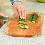 Mani femminili tagliano i cetrioli sul tagliere di legno