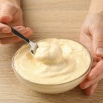 Mani femminili tengono cucchiaio e ciotola con la maionese