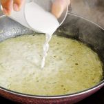 Padella sul fuoco con mano che versa latte di cocco