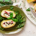 Fettine di rotolo di frittata su un piatto con rucola e basilico