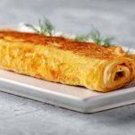 Rotolo di frittata farcito su piatto bianco con erbetta
