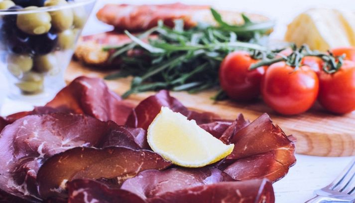 Bresaola e limone a tavola con pomodorini freschi, rucola e olive