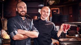 Lo Chef di una steakhouse mostra una bistecca cruda in cucina insieme al suo assistente
