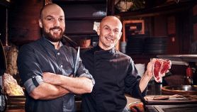 Lo Chef di una steakhouse mostra una bistecca cruda in cucina insieme al suo assistente