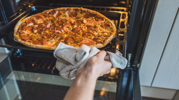 Mani femminili controllano la pizza nel forno