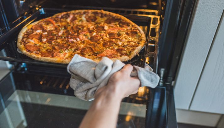 Mani femminili controllano la pizza nel forno