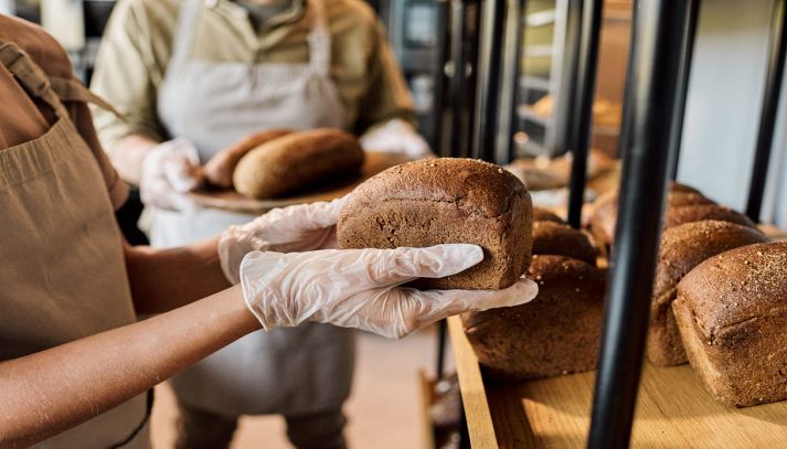Mani guantate reggono il pane nel panificio
