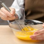 Mani di donna che sbattono le uova in una ciotola