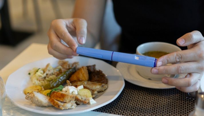 Una donna mangia porzioni ridotte in un ristorante mentre impugna una siringa portatile di Ozempic