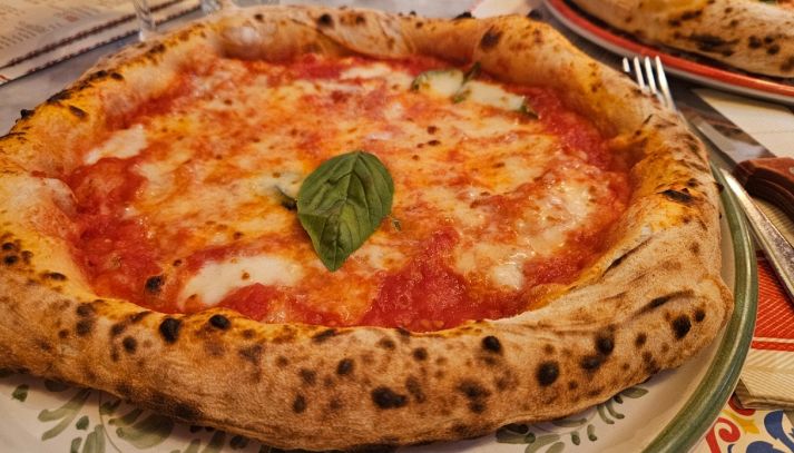 Il cornicione maculato di una pizza napoletana margherita con foglia di basilico
