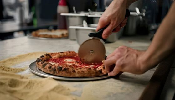 Una pizza napoletana con il cornicione a macchie scure viene tagliata con la rotella