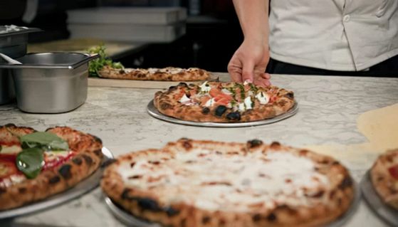 Pizzaiolo condisce la pizza nella cucina del ristorante