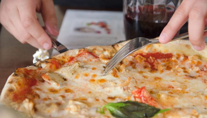 Mani tagliano pizza margherita con coltello e forchetta