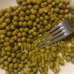 Piselli nel piatto che vengono schiacciati dalla forcheetta