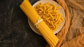 Un mazzo di spaghetti legati con un nastro su un piatto di fusilli pronti da cuocere