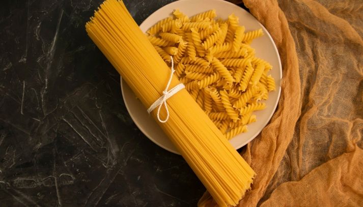 Un mazzo di spaghetti legati con un nastro su un piatto di fusilli pronti da cuocere