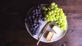 Un piatto con uva da tavola chiara e scusa e tocchetti di formaggio georgiano con coltello per spalmare.