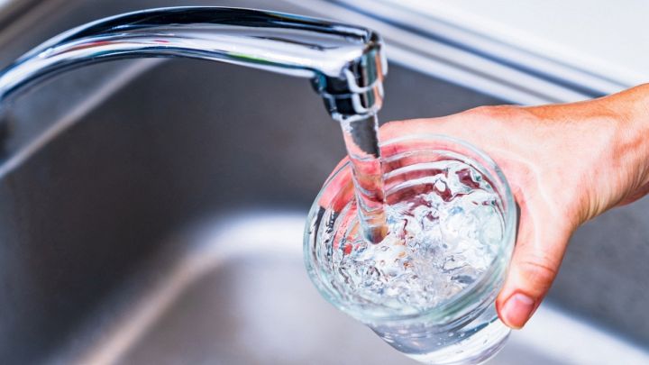 Una mano regge un bicchiere di acqua potabile che si riempie nel lavabo di casa