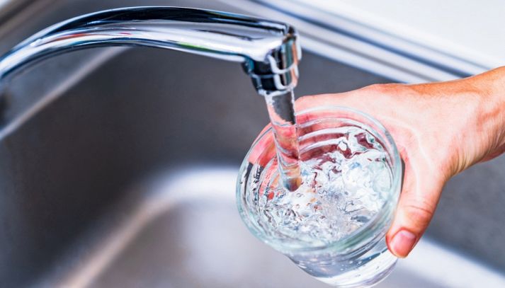 Una mano regge un bicchiere di acqua potabile che si riempie nel lavabo di casa