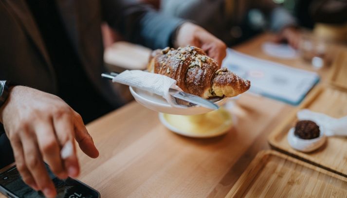 Cliente con un croissant ripieno di gelato si siede al tavolino di un bar