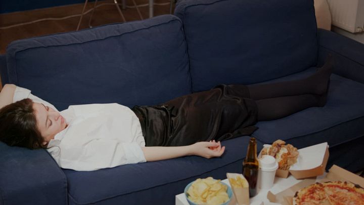 Donna che dorme sul divano con tanto cibo spazzatura
