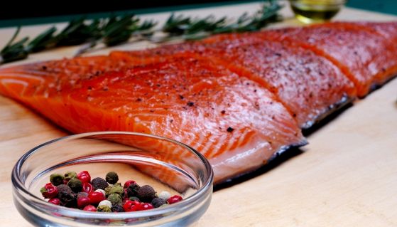 Filetto di salmone affumicato su tagliere con ciotola di grani di pepe