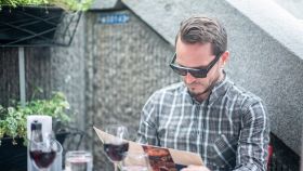 Uomo seduto al tavolo del ristorante esamina il menù indossano un paio di occhiali da sole smart