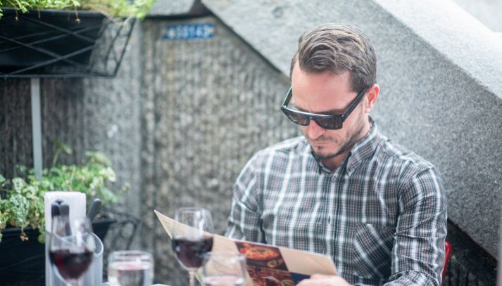 Uomo seduto al tavolo del ristorante esamina il menù indossano un paio di occhiali da sole smart