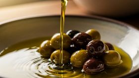 Un filo di olio extravergine viene versato in un piato con delle olive da tavola