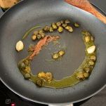 Padella in cui soffriggono capperi, aglio e acciughe nell'olio