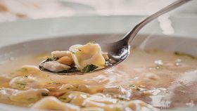 Cucchiaio con tortellino in brodo e piatto sullo sfondo