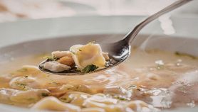 Cucchiaio con tortellino in brodo e piatto sullo sfondo