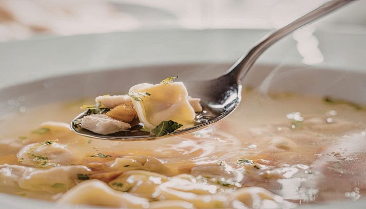 Cucchiaio con tortellino in brodo e piatto sullo sfondo