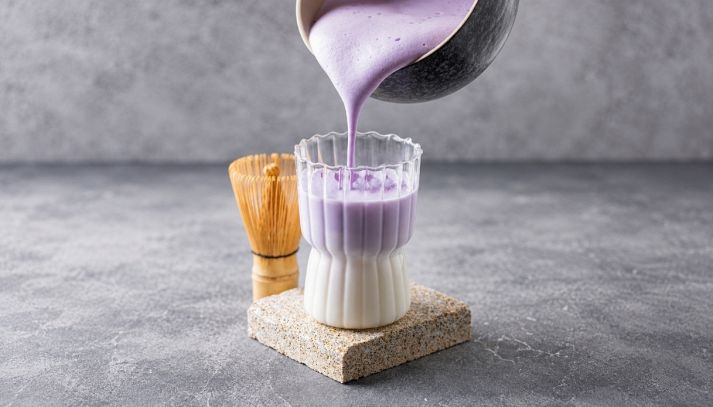 Un bricco versa ube latte appena miscelato e spumoso in un bicchiere