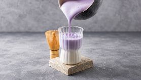 Un bricco versa ube latte appena miscelato e spumoso in un bicchiere